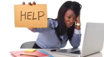 Woman holding "help" sign sitting at computer